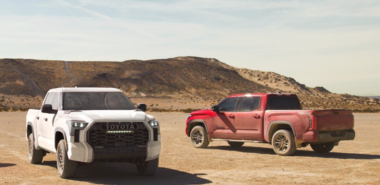 A white and red 2025 Toyota Tundra parked in a desert facing opposite directions and covered in dirt