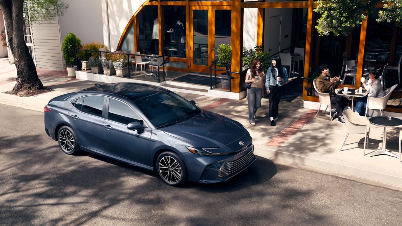A blue Toyota Camry parked by the curb outside a coffee shop