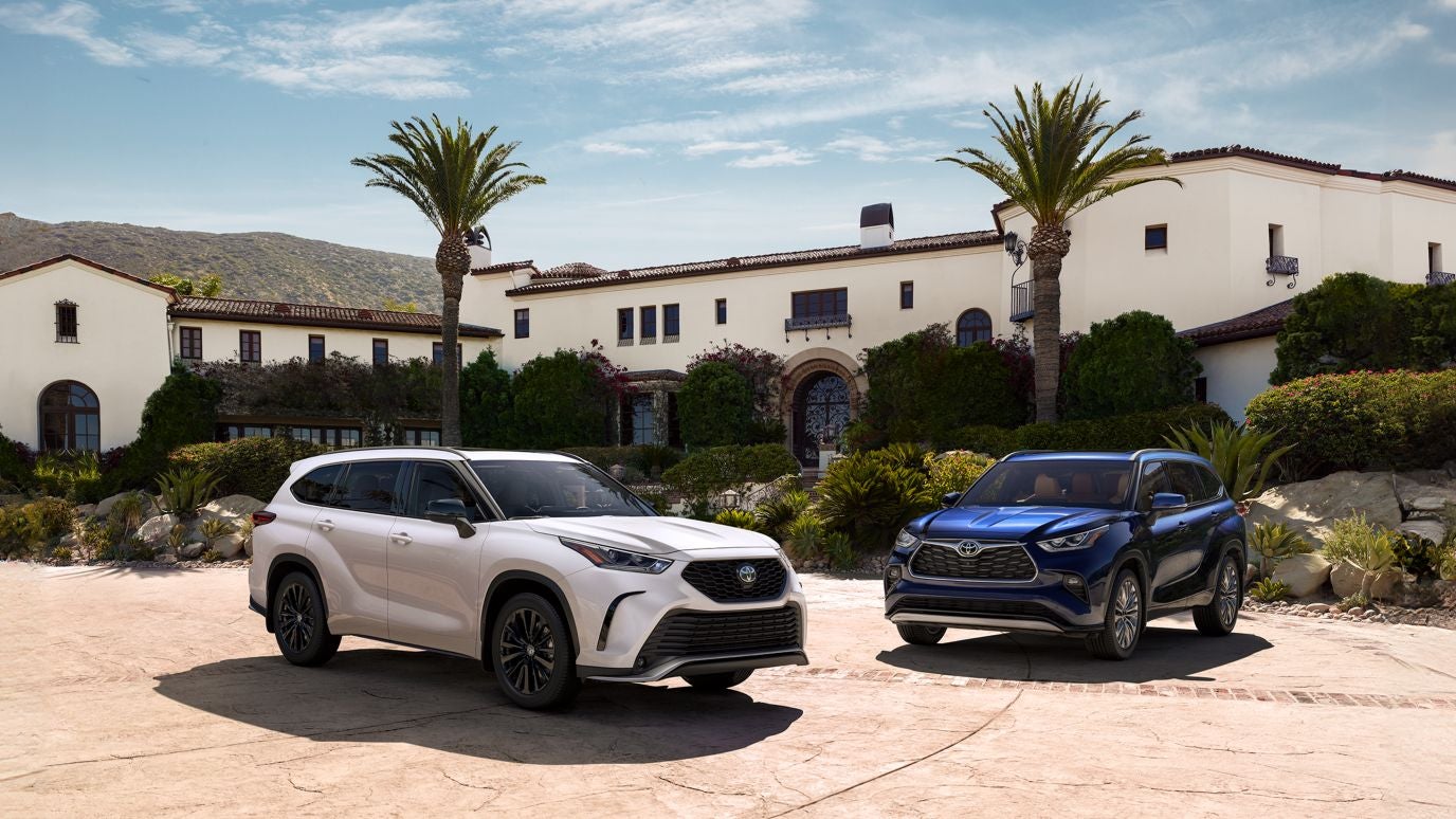 Two Toyota Grand Highlanders, one white and one blue, parked outside of a large house
