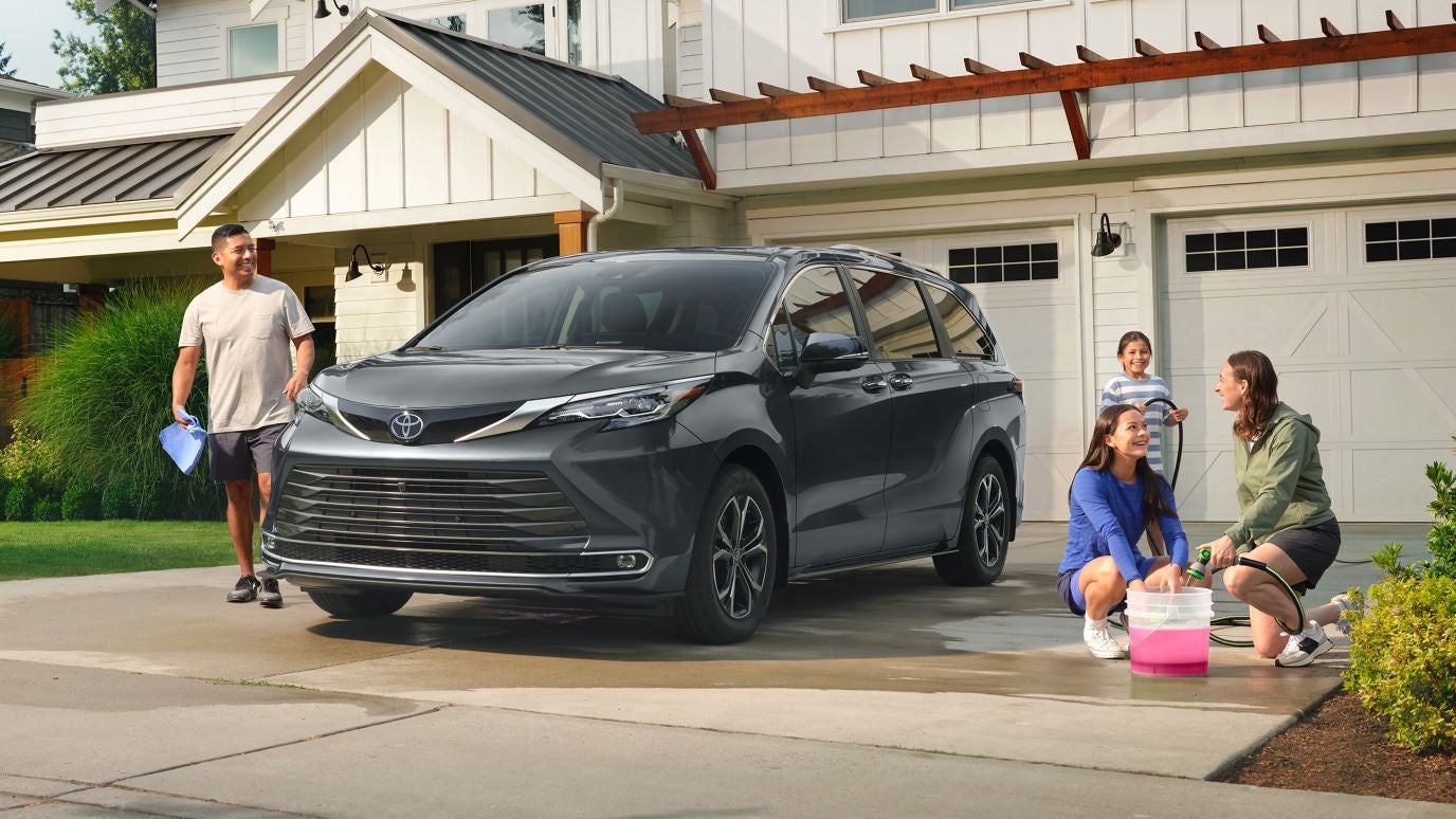 A dark gray Toyota Sienna being washed by a family in their driveway