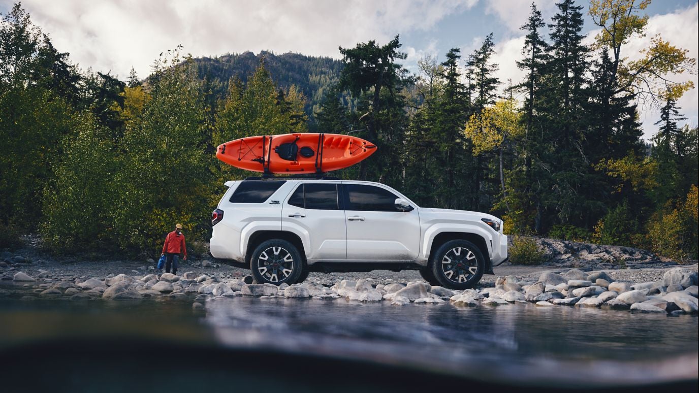 A white Toyota 4Runner in profile parked at a lake bed with an orange kayak strapped to its roof