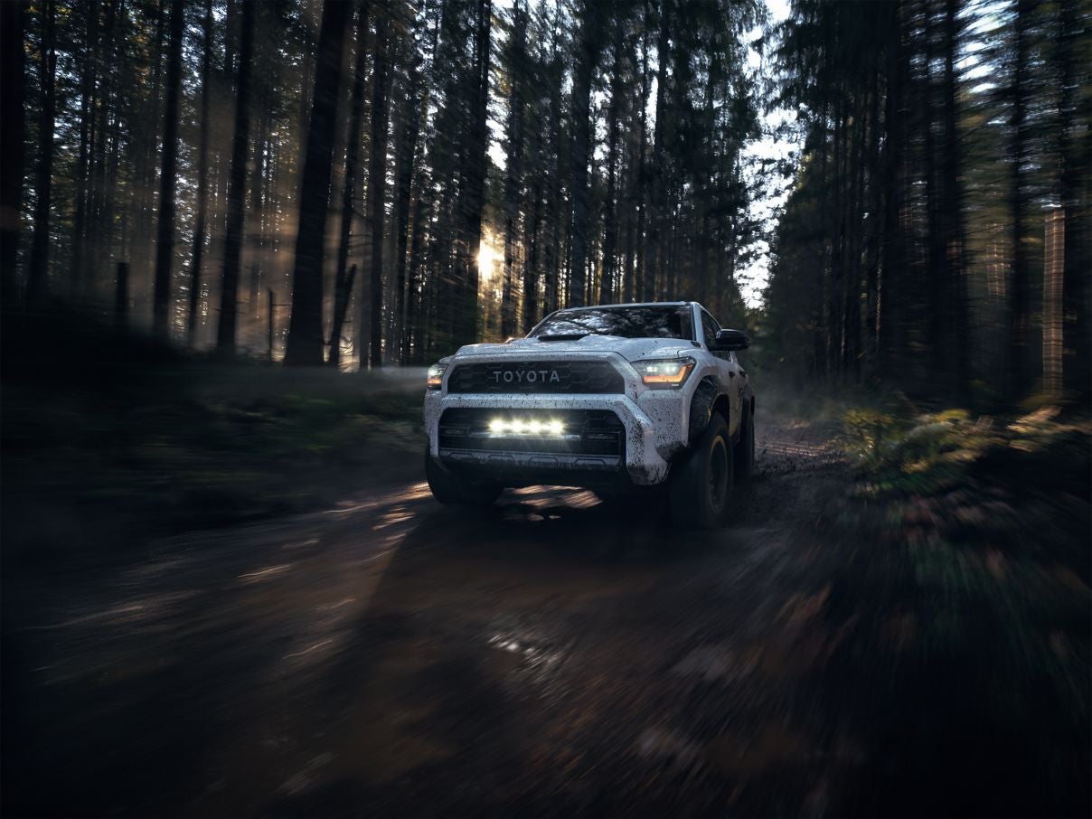 A white speckled Toyota 4Runner driving over a dirt road through a forest