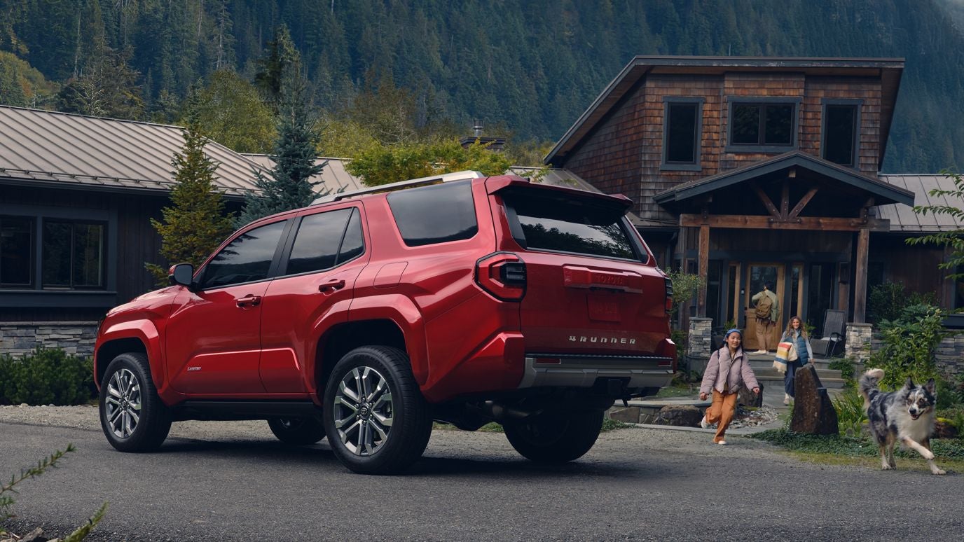A red Toyota 4Runner parked outside a cabin with a family and dog running by it