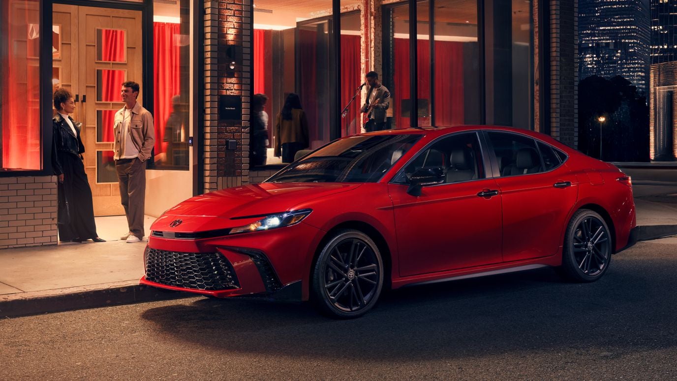 A red Toyota Camry parked by the curb at night outside a club or restaurant