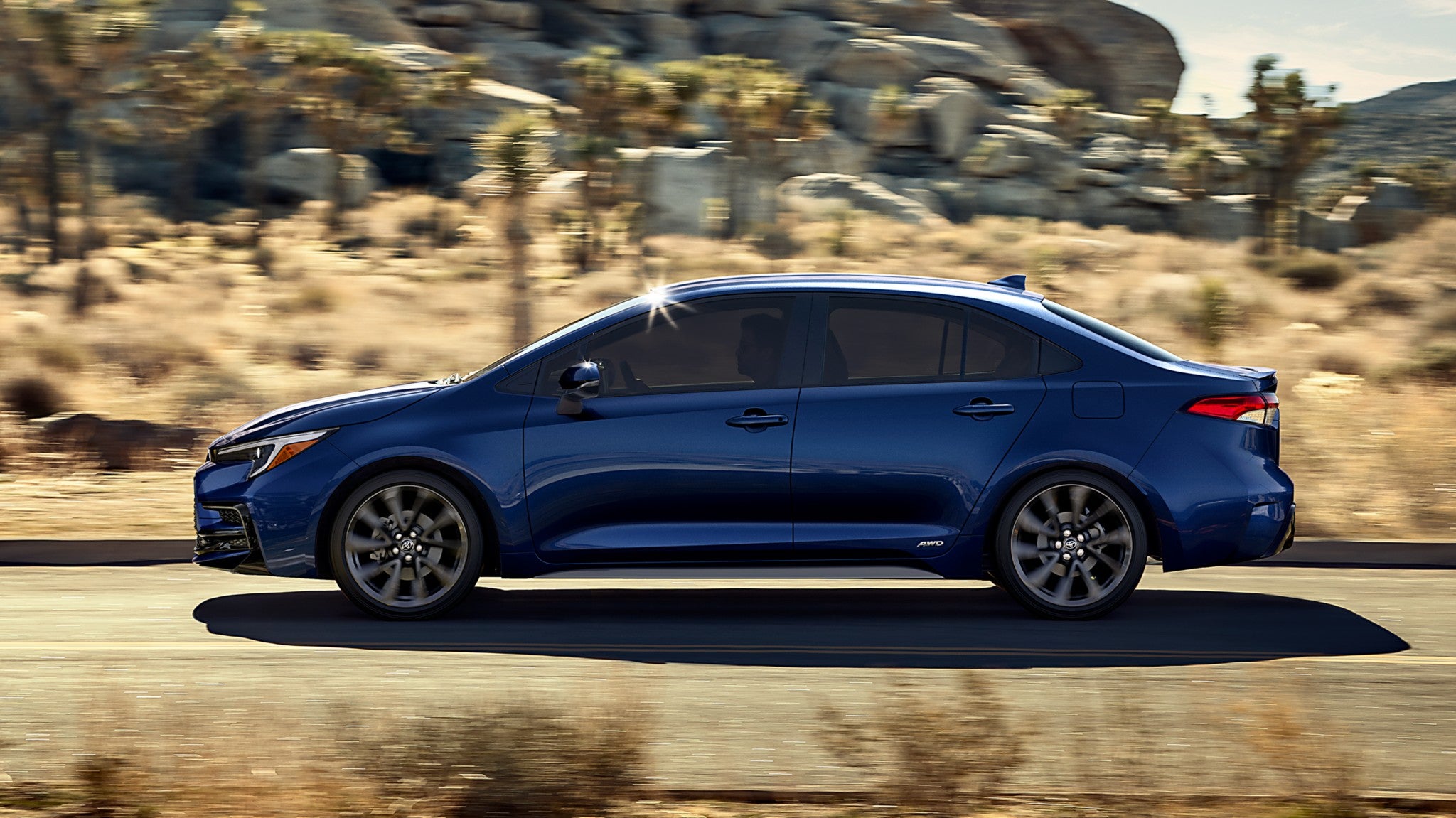 A blue Toyota Corolla driving down the road in the desert