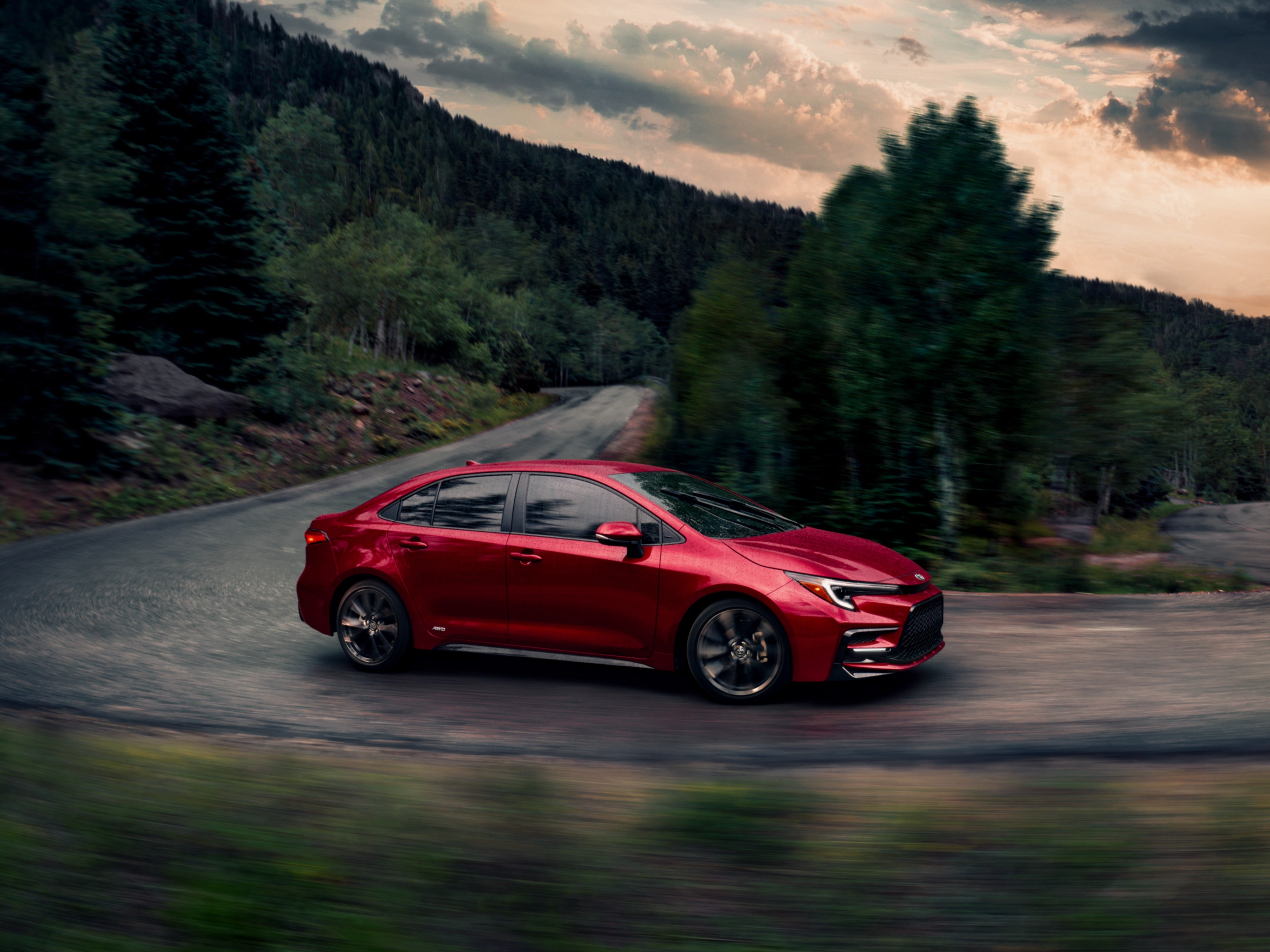 A red Toyota Corolla driving around a bend through a forested area