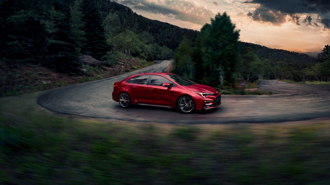 A red Toyota Corolla drink around a bend cutting through a forest