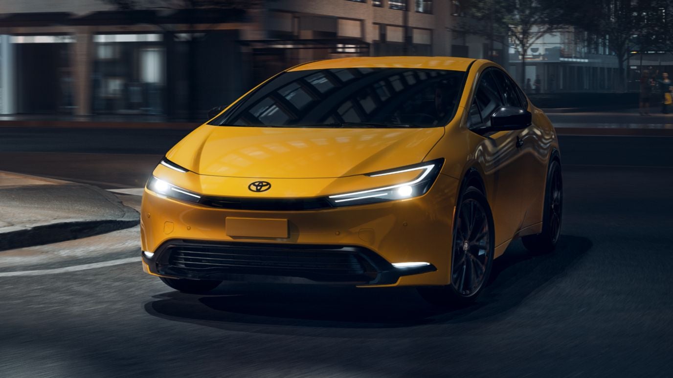 A yellow Toyota Prius driving down the street at night