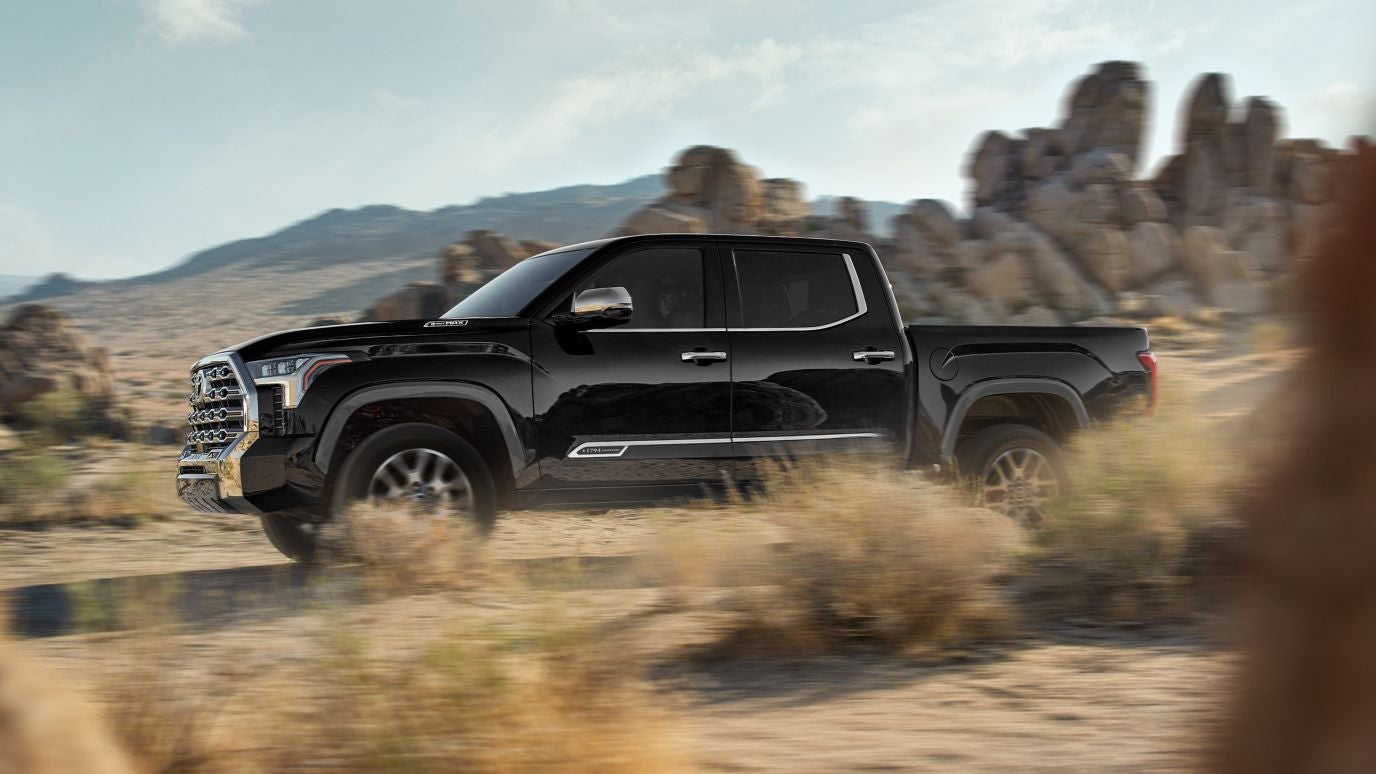 A black Toyota Tundra in profile driving off-road through a desert.