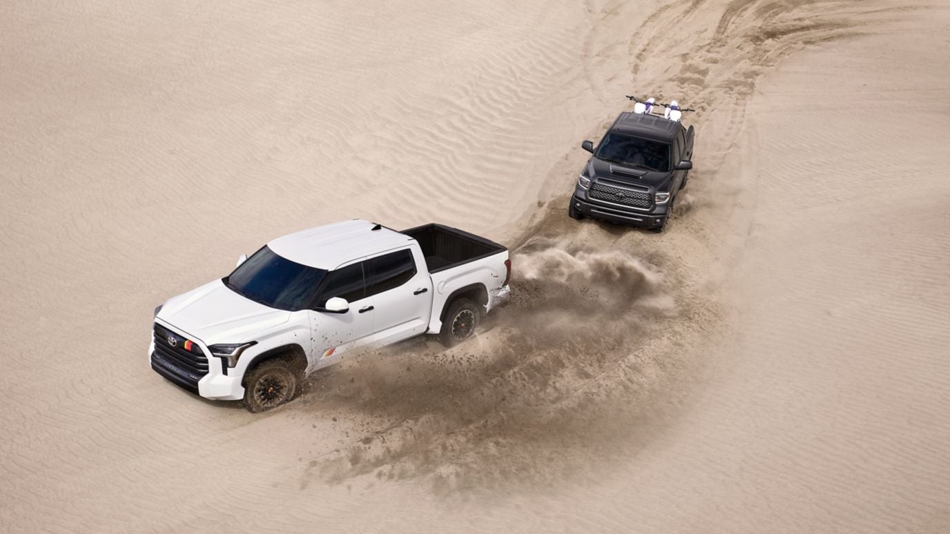 An overhead view of a white and a black Toyota Tundra driving through desert sands