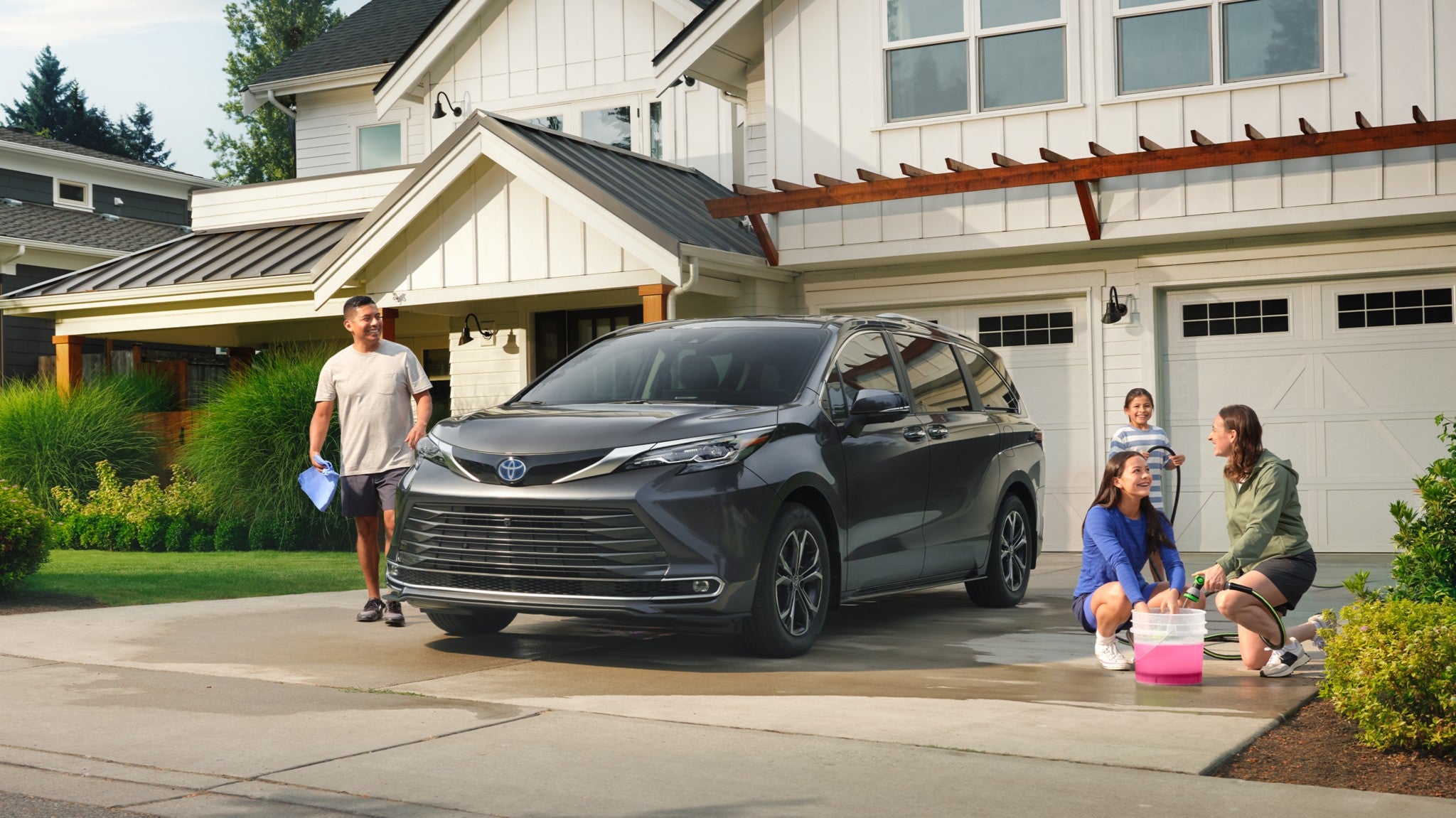 A dark gray Toyota Sienna in a driveway being washed by a family