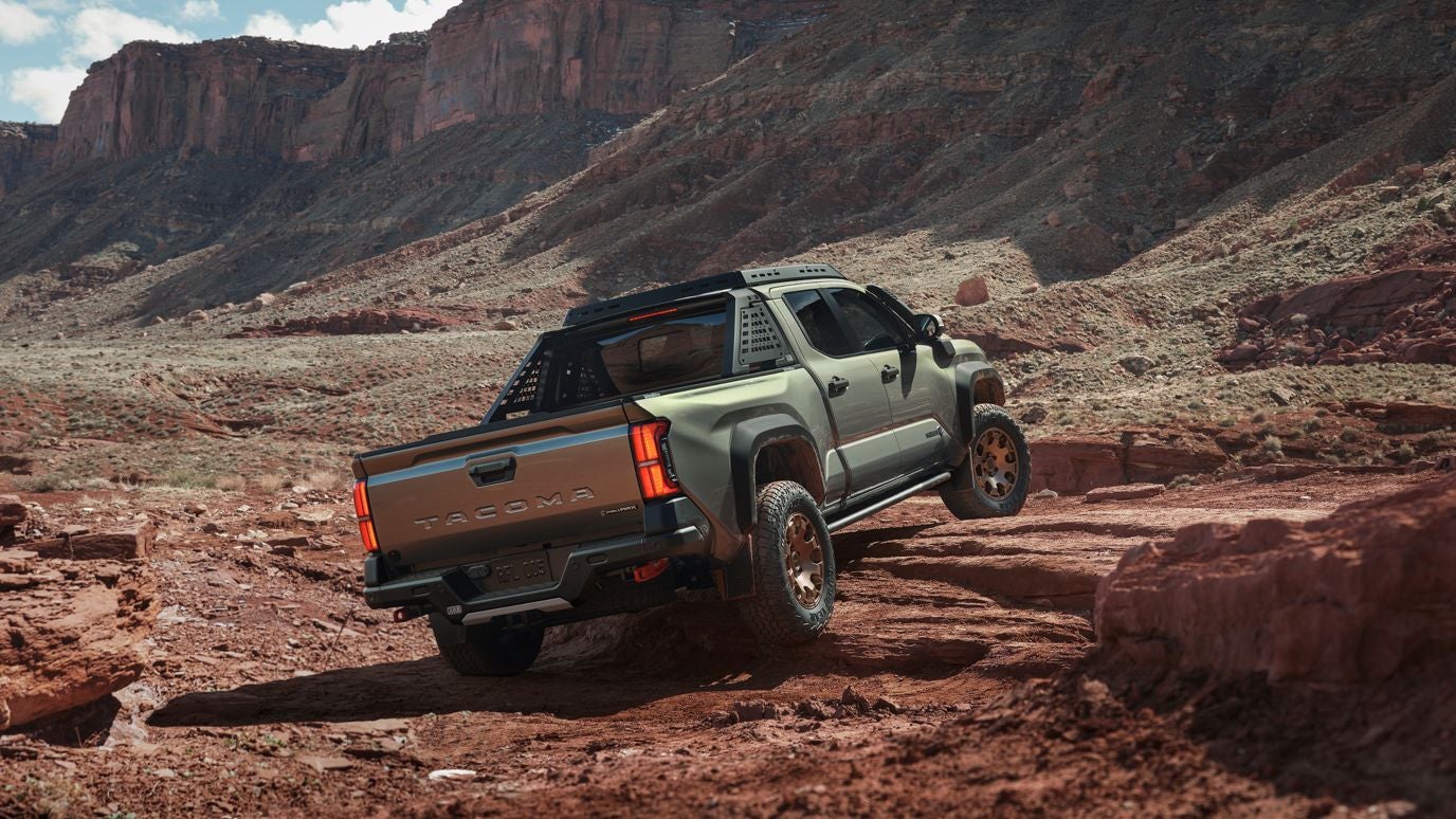 A rear view of a green Toyota Tacoma driving over rocky hills