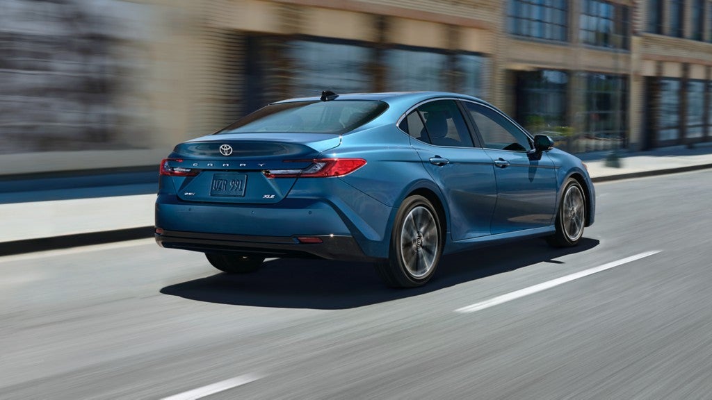 A blue 2025 Toyota Camry quickly driving through a city