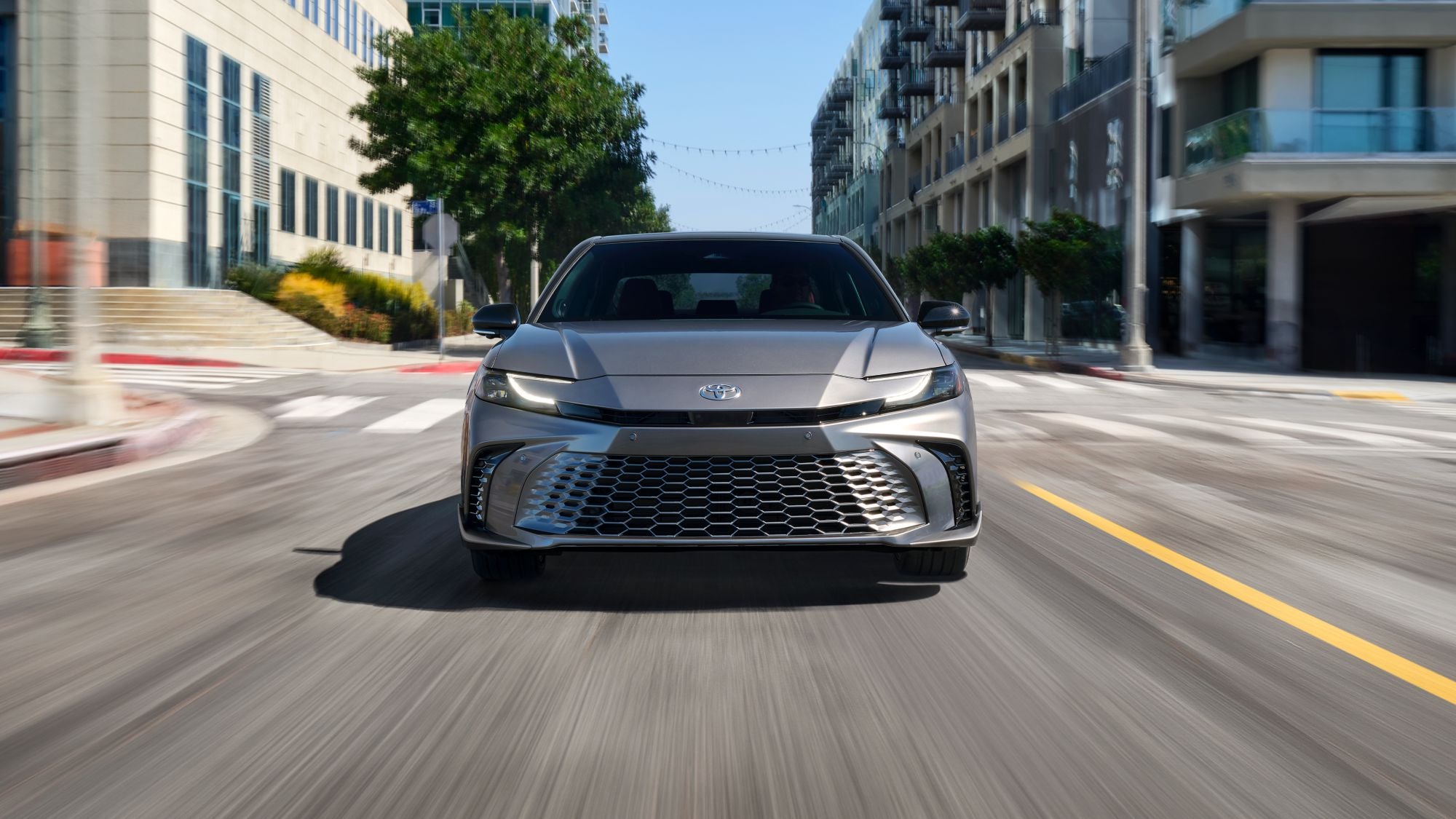 A front view of a silver Toyota Camry driving down the street
