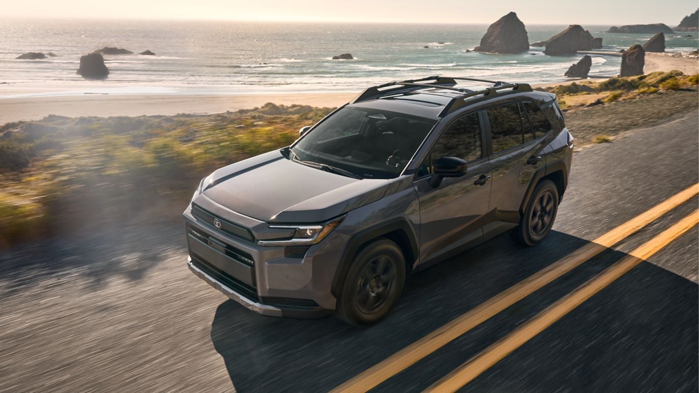 A gray Toyota RAV4 driving down the road by a beach