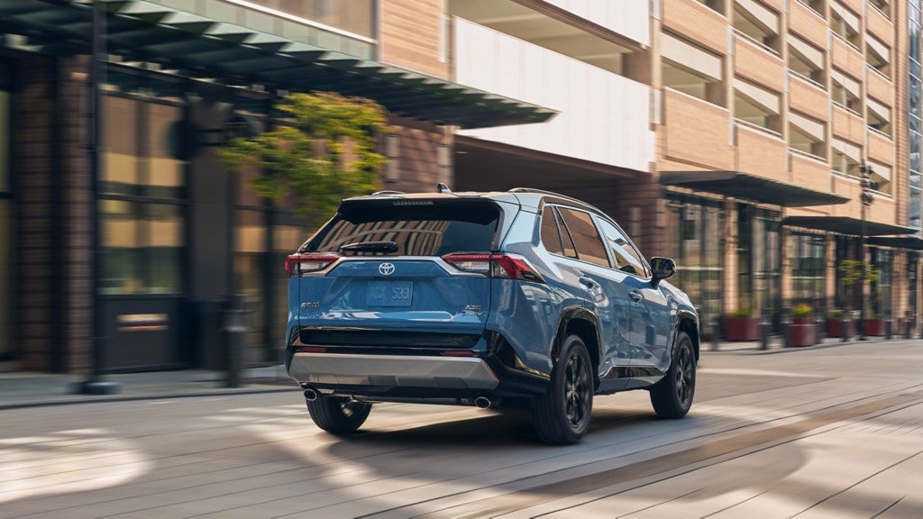 A rear view of a blue Toyota RAV4 Hybrid driving through a city