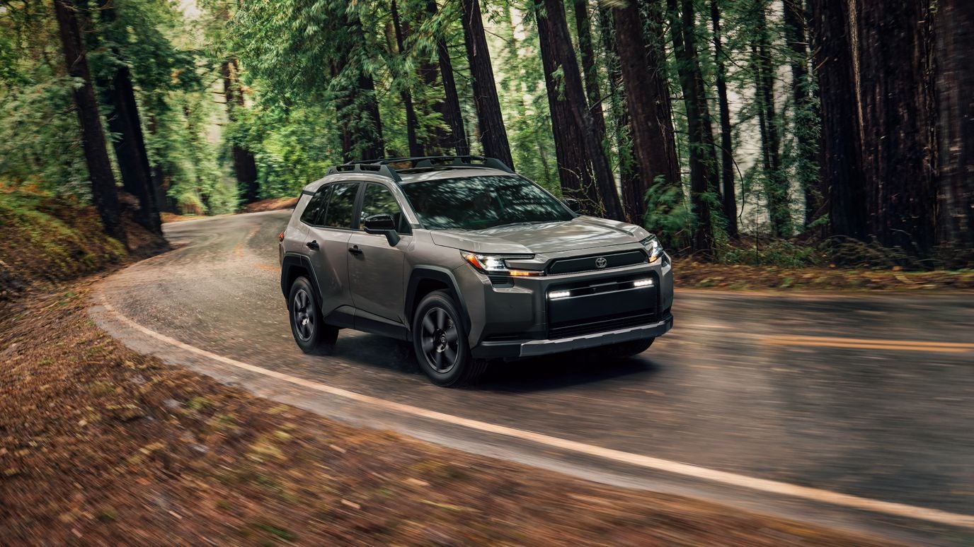 A grey Toyota RAV4 driving along a winding road in a forest