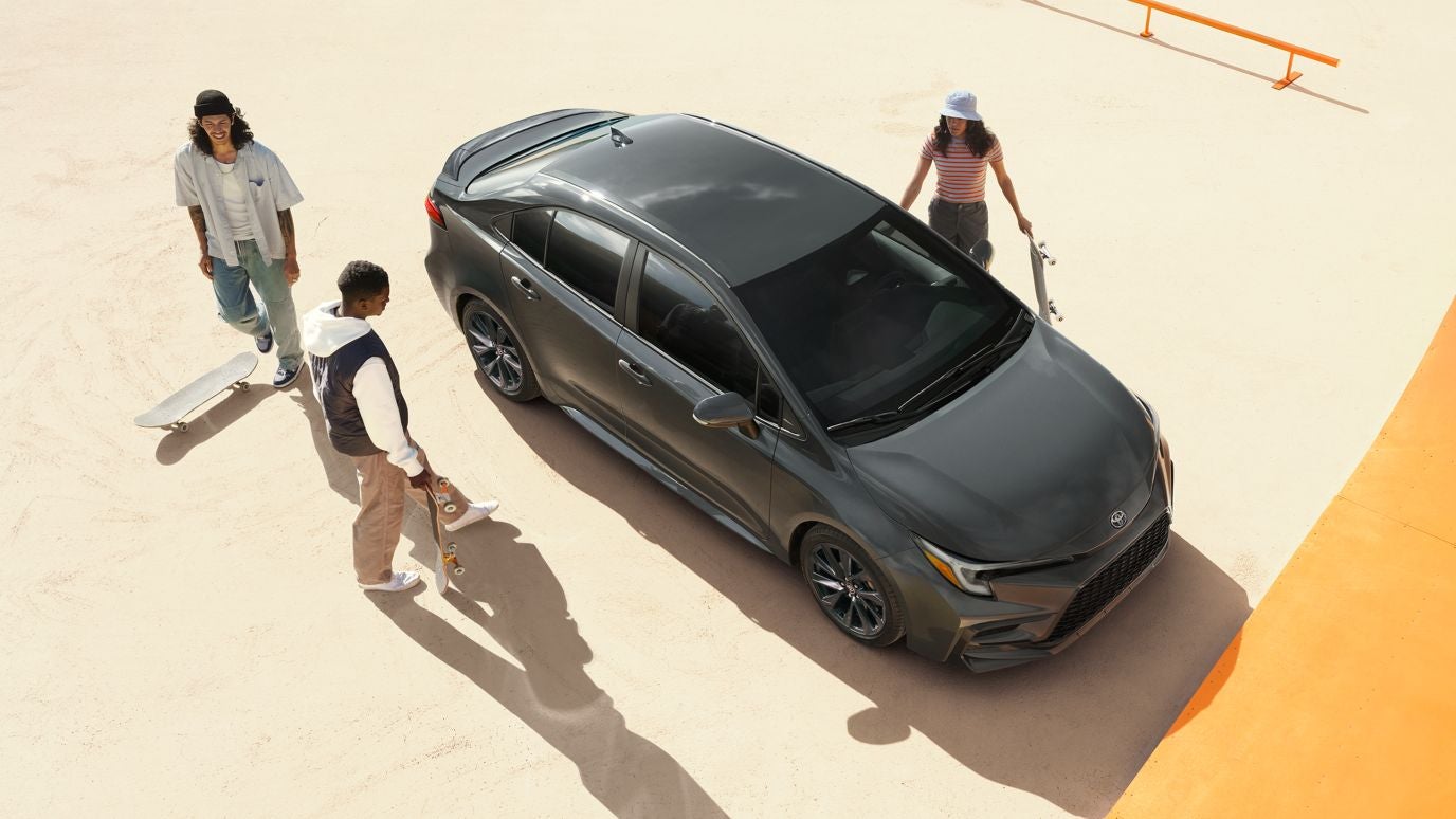 An overhead view of a gray Toyota Corolla with three people around it in a skate park
